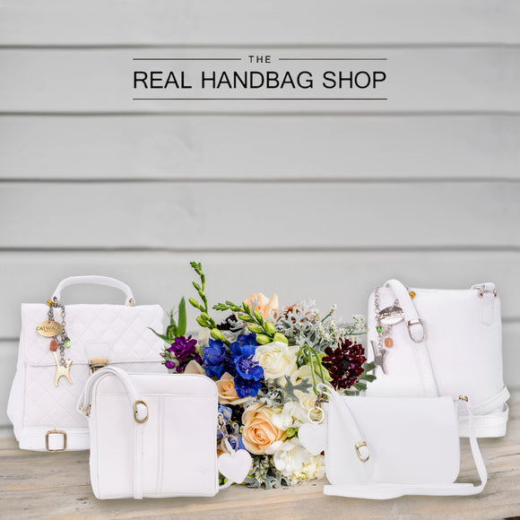 Collection of white leather handbags and crossbody bags next to a bunch of flowers.